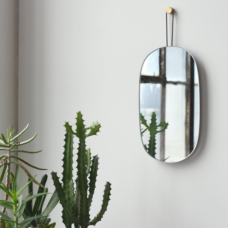 Brass-Hung Oval Wall Mirror — Oval glass mirror with dark metal strap and brass-tone wall pin