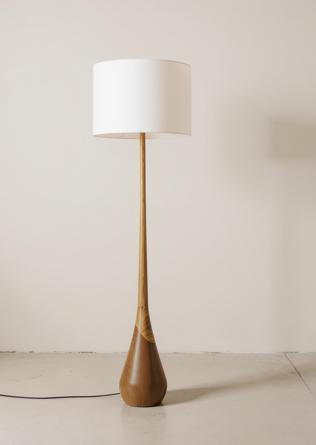 Two-tone wood floor lamp with a white drum shade and teardrop-shaped base in a neutral studio.