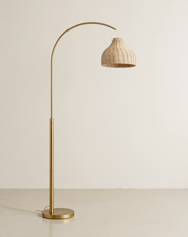 Brass arc floor lamp with a hanging wicker bell shade and round base