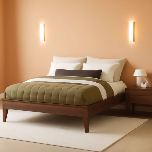 Dark brown platform bed with green bedding beside wall sconces in a warm beige bedroom.