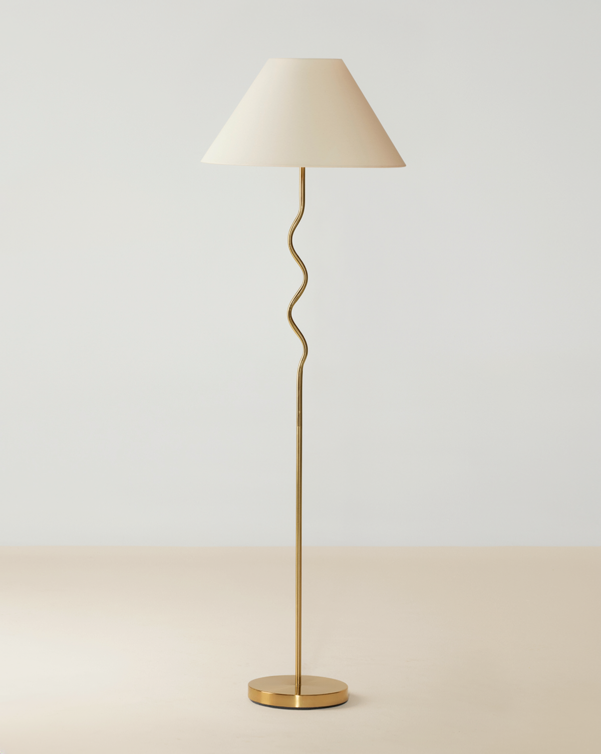 Brass floor lamp with a wavy stem, cream tapered shade and round brass base.