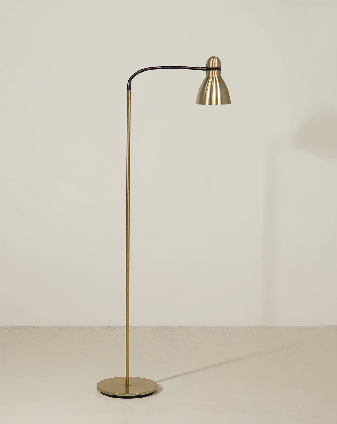 Brass floor lamp with a black flexible gooseneck, bell task shade and round base.