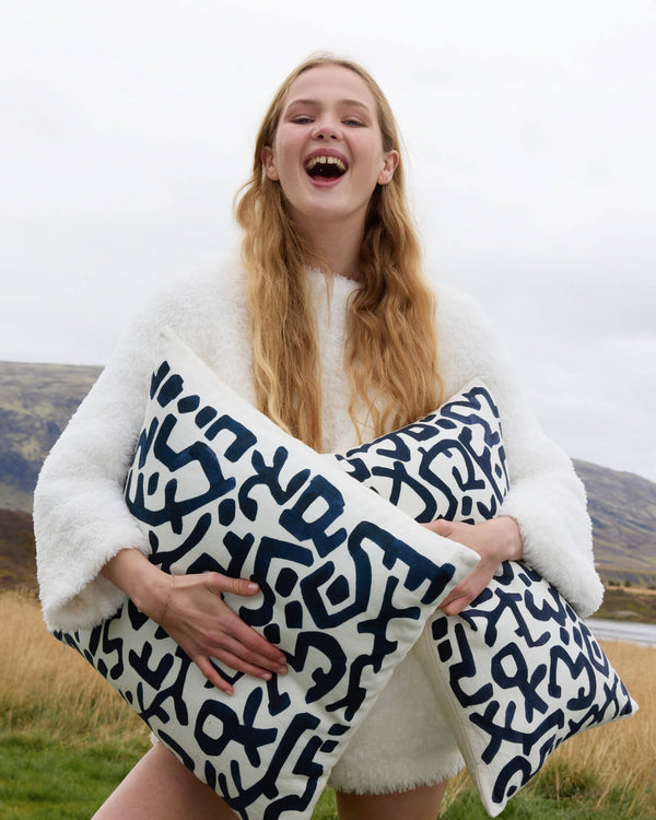 Woman holding a white blanket with blue geometric patterns in a scenic outdoor setting