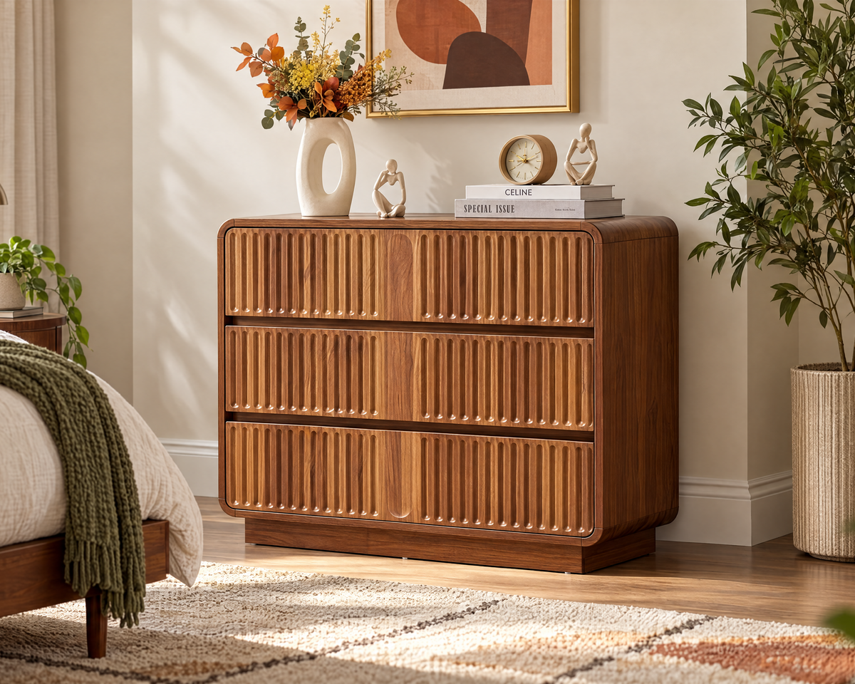 A mid-century modern wooden chest of drawers in a warm medium brown finish, styled in a bright bedroom next to a bed and a potted plant.