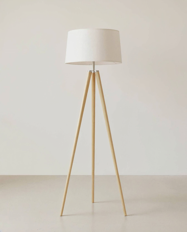 Natural wood tripod floor lamp with linen shade against a chalk off-white wall and pale concrete floor