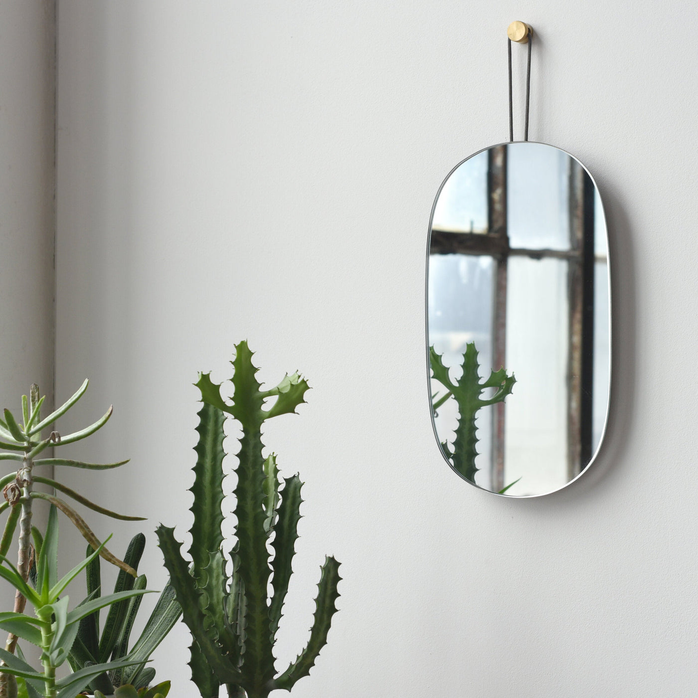 Brass-Hung Oval Wall Mirror — Oval glass mirror with dark metal strap and brass-tone wall pin
