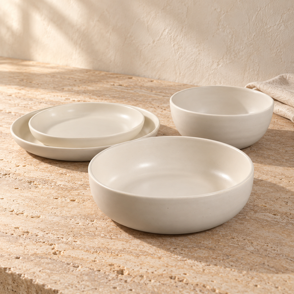 Matte Ivory Ceramic Dinnerware Set — Set of all four pcs., arranged on pale travertine in warm natural light