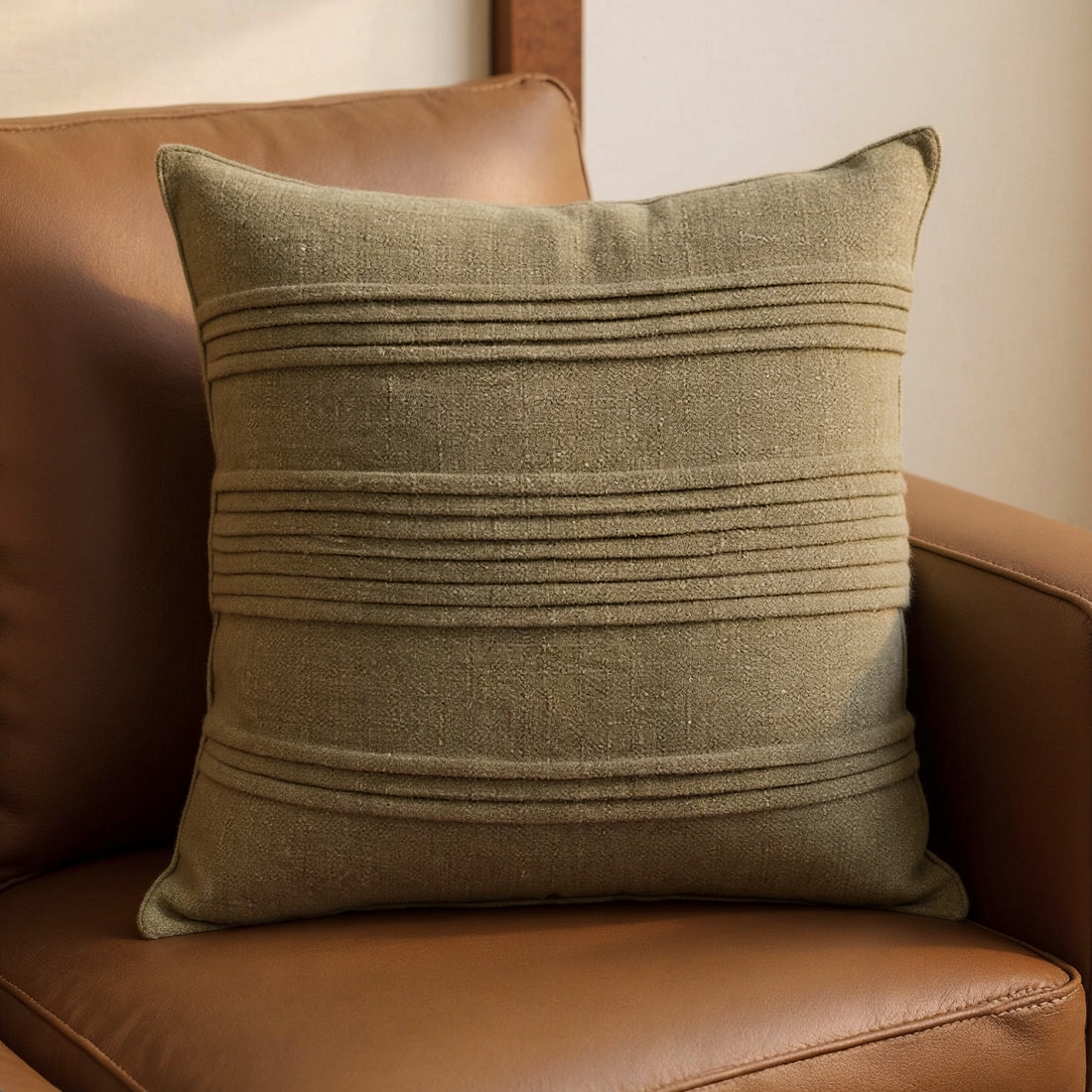 Moss Green Pintuck Linen-Blend Pillow Cover with horizontal pintuck bands on a cognac leather lounge chair
