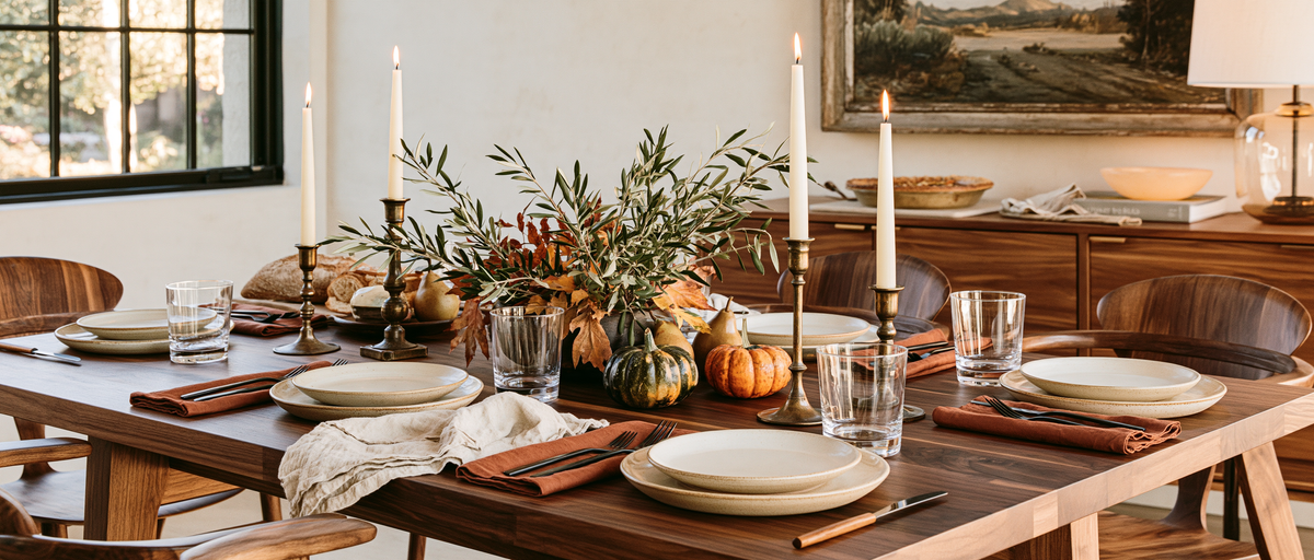 A Thanksgiving table with ivory plates, linen napkins, candlelight, and autumn foliage