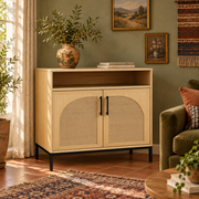 Light wood buffet cabinet with arched rattan doors, black pulls and a slim black base in a Boho room with olive walls and terracotta flooring