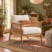 Cream-cushioned braided cord wood-frame accent chair with a rust striped pillow in a Boho room with olive walls and layered patterned rugs