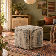 Beige cube pouf with chunky cream, dusk-blue and taupe woven stripes beside an olive sofa on layered patterned rugs in a Boho living room