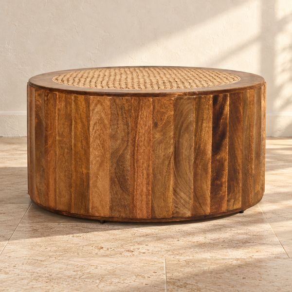 Round Mango Wood Rattan Coffee Table against a cream limewash wall on a travertine floor in warm afternoon light
