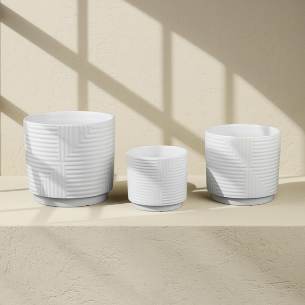 Geometric Relief Stoneware Planter Set against cream microcement with warm steel-window grid shadows