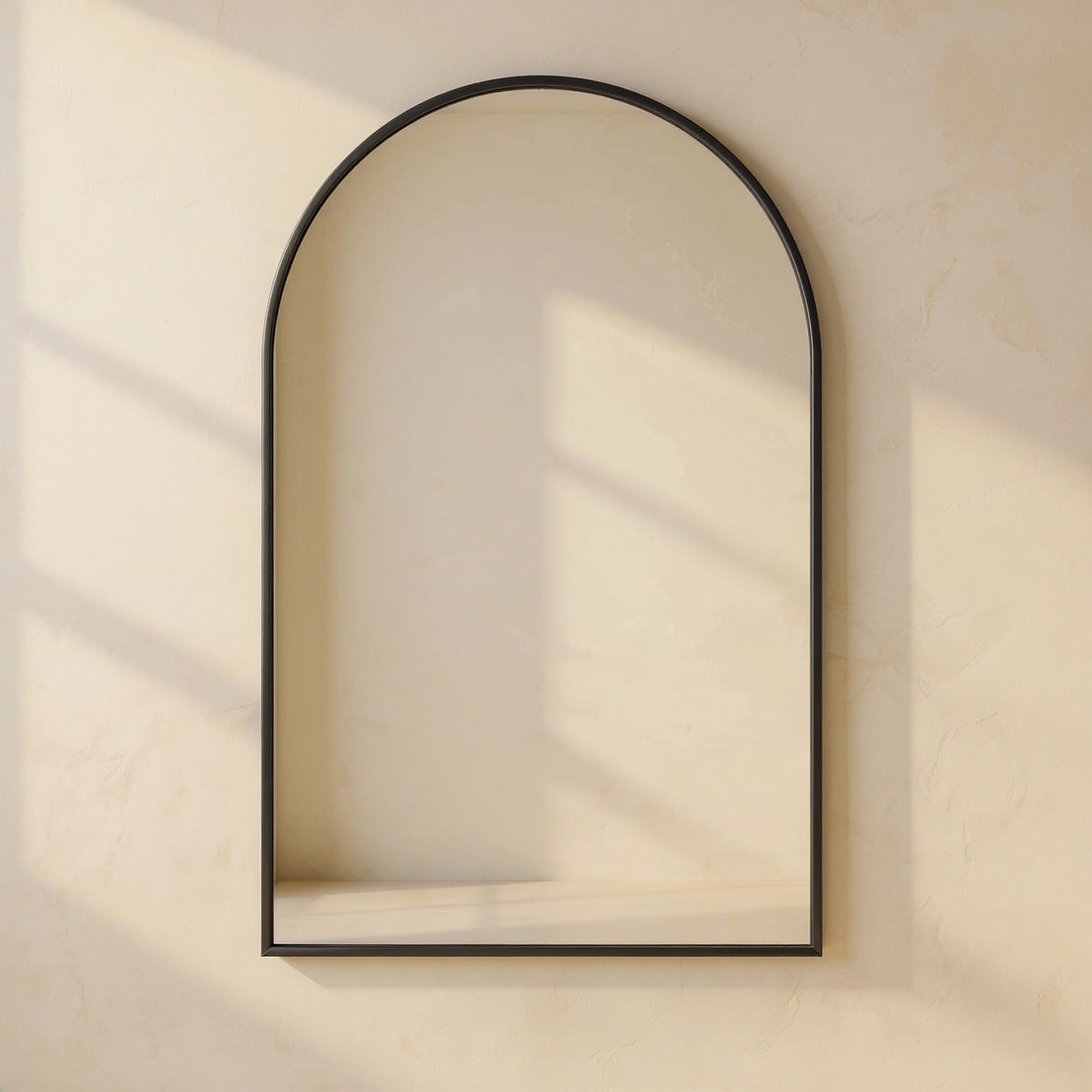 Arched Matte Black Metal Wall Mirror against a cream limewash wall with warm natural side light.