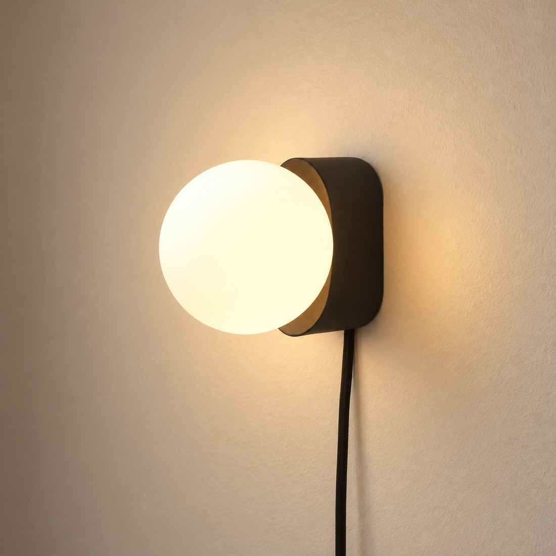 Globe Glass Metal Wall Sconce illuminated against cream plaster