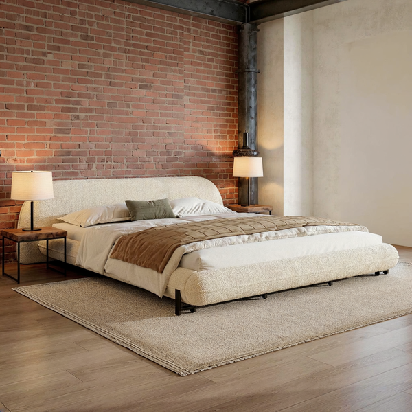 Curved cream bouclé California king bed with ivory bedding in a brick and steel loft bedroom with a flat oatmeal rug.