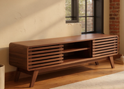 Walnut 59-Inch Mid-Century TV Stand with Storage beside a sunlit loft window, showing slatted doors and open shelves