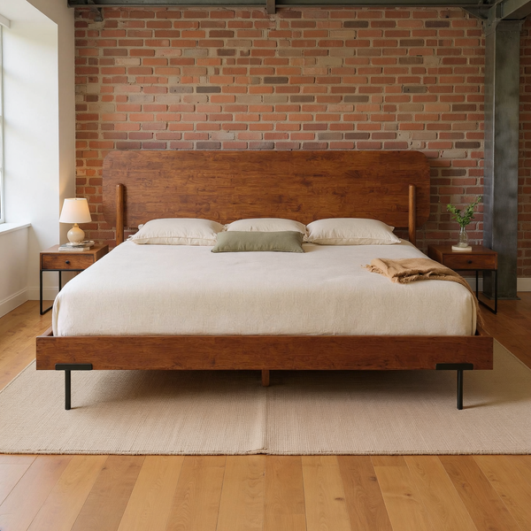 Rounded walnut headboard platform bed with slim black metal legs, ivory bedding, olive pillow and camel throw in a warm brick loft bedroom on a flat oatmeal rug.
