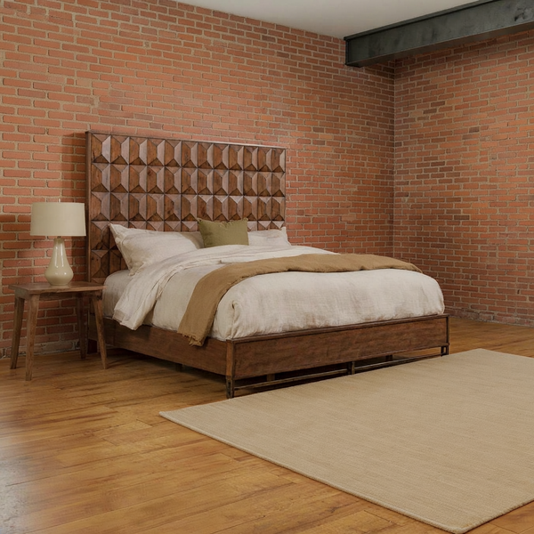 Brown faceted wood headboard with ivory bedding, an olive cushion and a camel throw in a brick loft bedroom with a flat oatmeal rug.