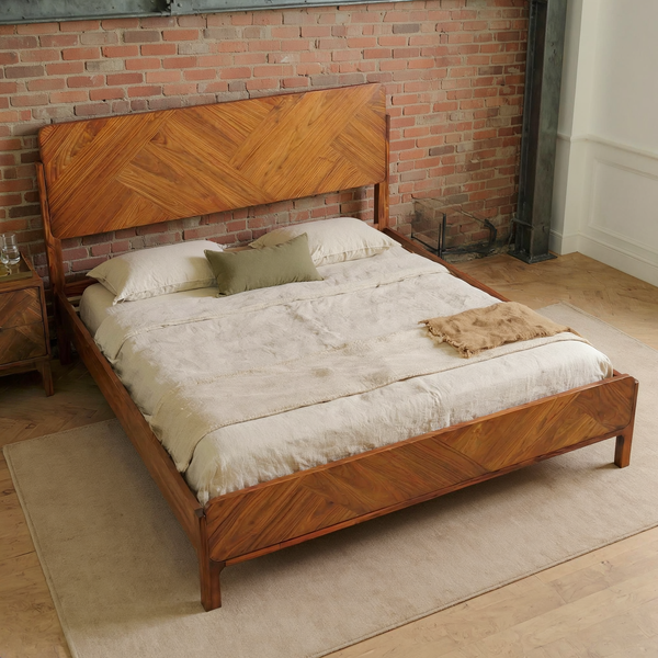 Geometric Parquet Wood Bed Frame with ivory bedding and a camel throw, shown at an angle in a warm brick and steel loft bedroom with a flat oatmeal rug.