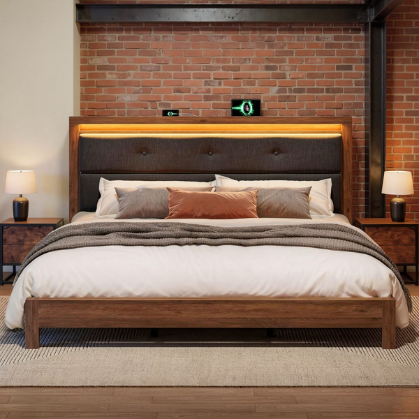 Wood and charcoal upholstered king bed with its LED charging headboard, layered ivory bedding, gray blanket and terracotta pillow in a brick loft bedroom.