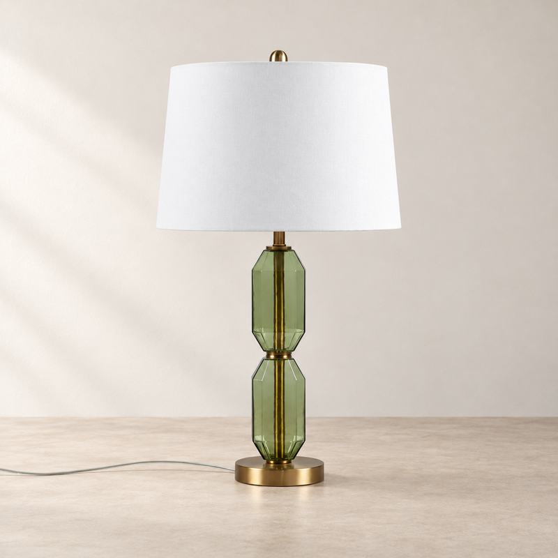 Faceted green glass table lamp with a white drum shade on a neutral tabletop