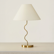 Brass squiggle-stem table lamp with cream fabric shade on a neutral concrete tabletop
