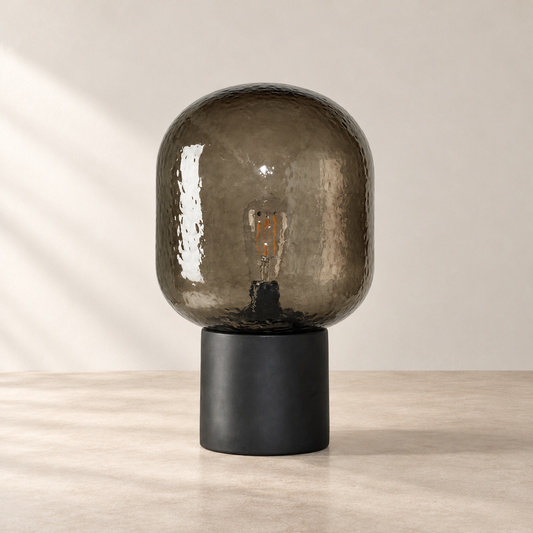Smoked glass dome table lamp with a charcoal cylindrical base on a warm neutral surface
