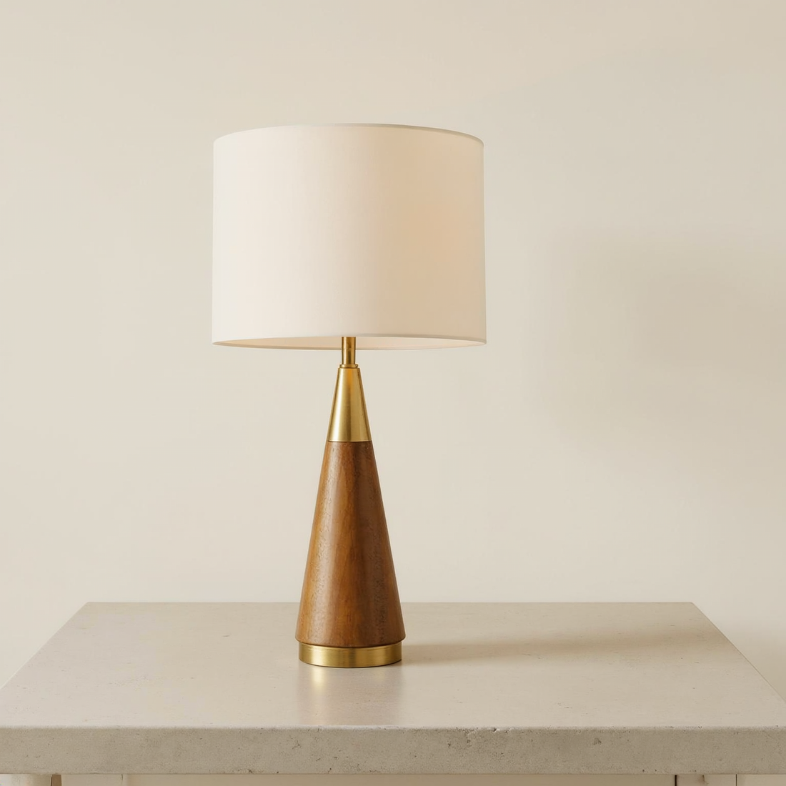Cone base brass and wood table lamp with a cream drum shade on a neutral tabletop