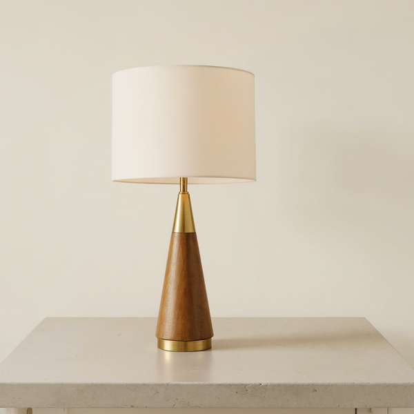Cone base brass and wood table lamp with a cream drum shade on a neutral tabletop
