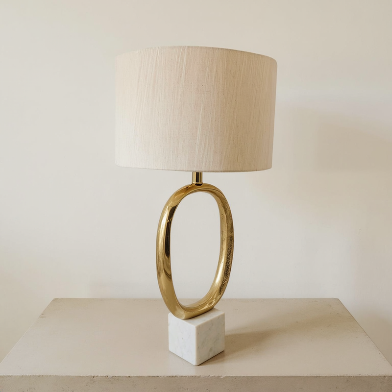 Oval gold metal table lamp with a cream drum shade on a neutral tabletop