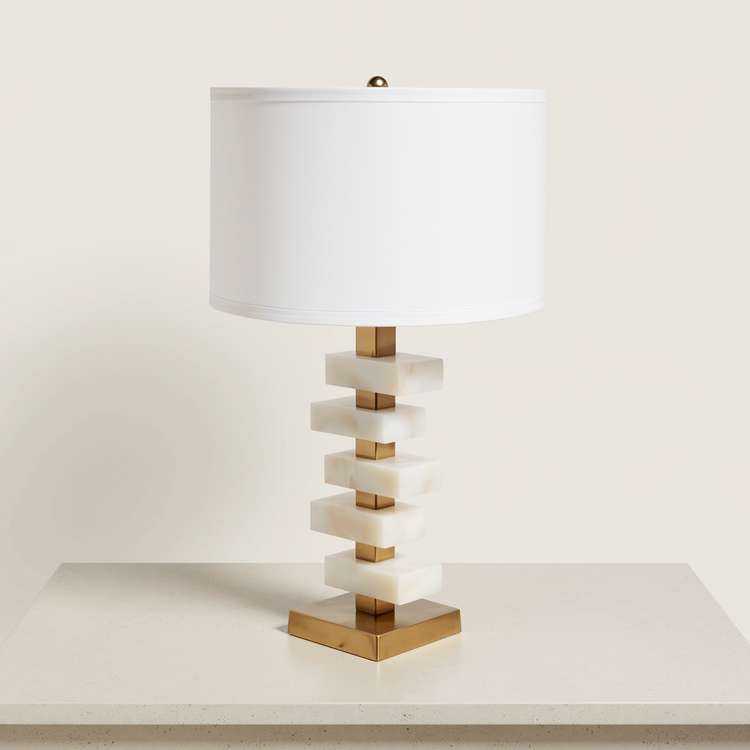 Stacked alabaster slab table lamp with a white drum shade and brass base on a neutral tabletop