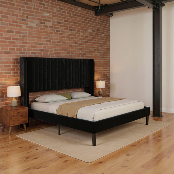 Black velvet wingback queen bed with vertical channels, ivory bedding and camel throw, shown at an angle in a brick and steel loft bedroom on a flat oatmeal rug.