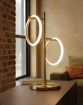 Brass Saturn table lamp with two illuminated rings on a walnut console in a warm brick loft
