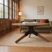 Solid walnut round coffee table with black steel bracket and splayed walnut legs in a sunlit brick loft